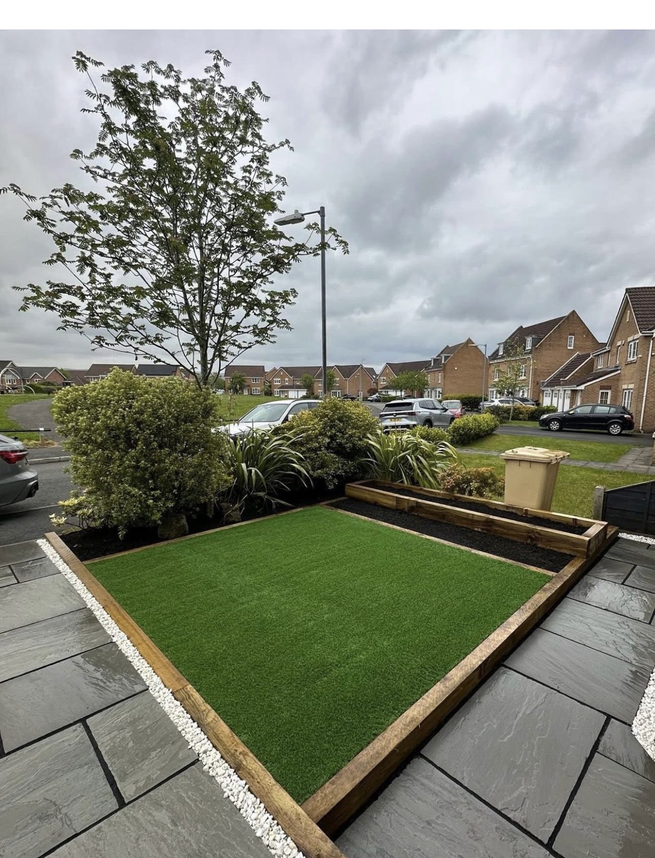 Artificial grass lawn framed with timber sleepers and slate paving on a front garden in Bolton