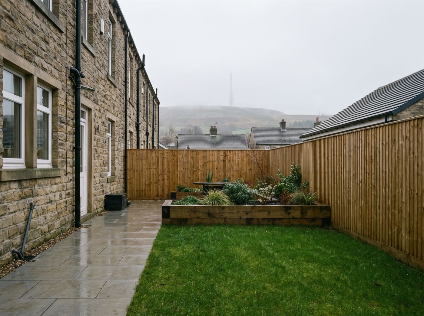 Long terraced back garden in Horwich after landscaping: porcelain patio, lawn, new fence and raised bed, Winter Hill beyond (illustrative)